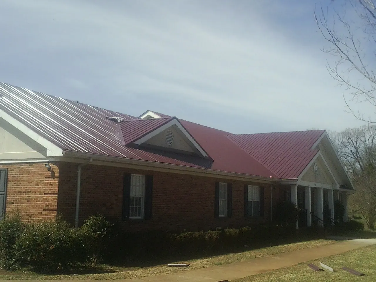 Red metal roof with gabled entries on a long brick building, from a Hail Damage Roof Repair job in Mineral Wells