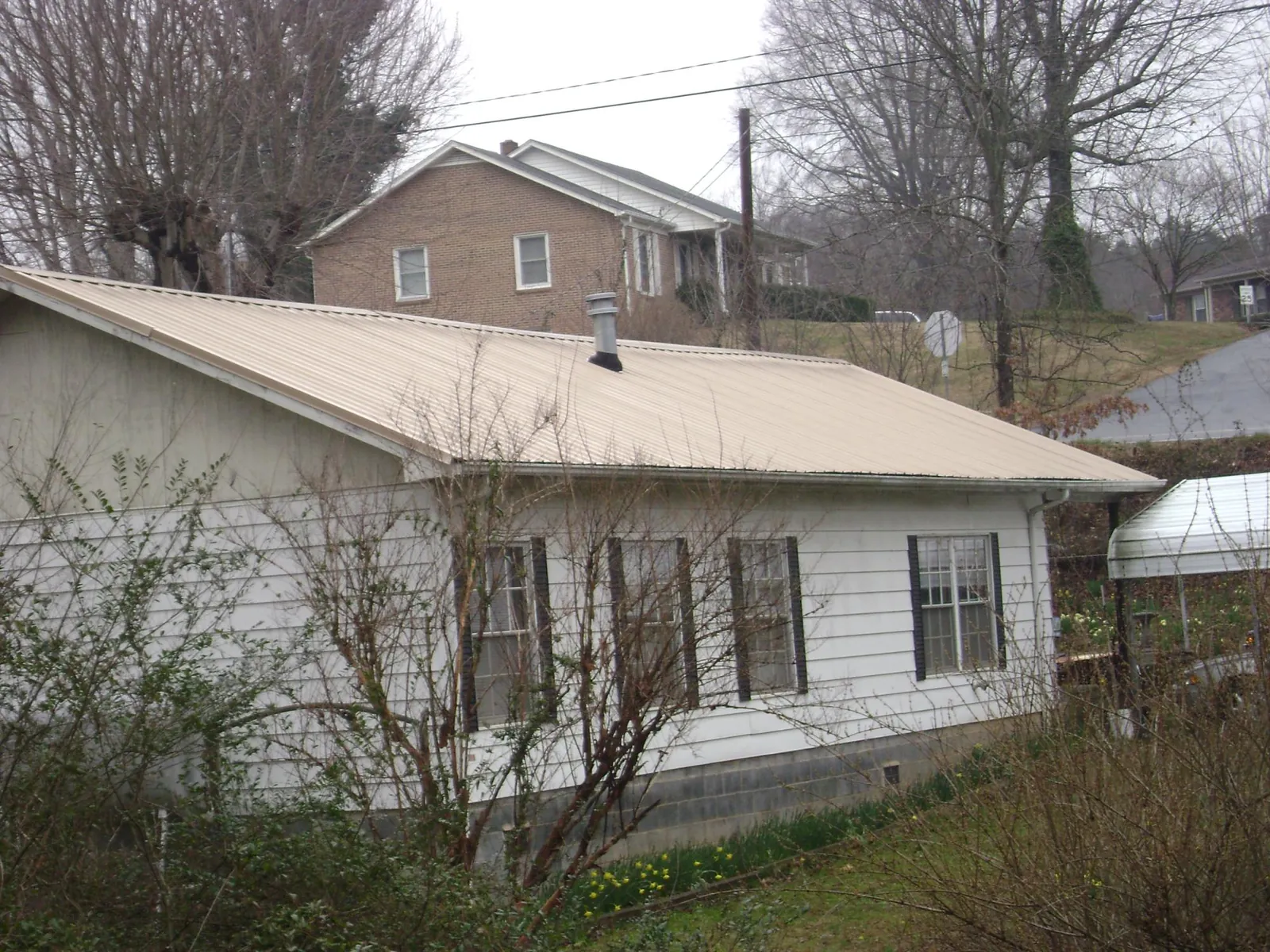 Tan metal roof on a white sided house set into a hillside — Commercial Roofing by Roofing Brothers in Mineral Wells