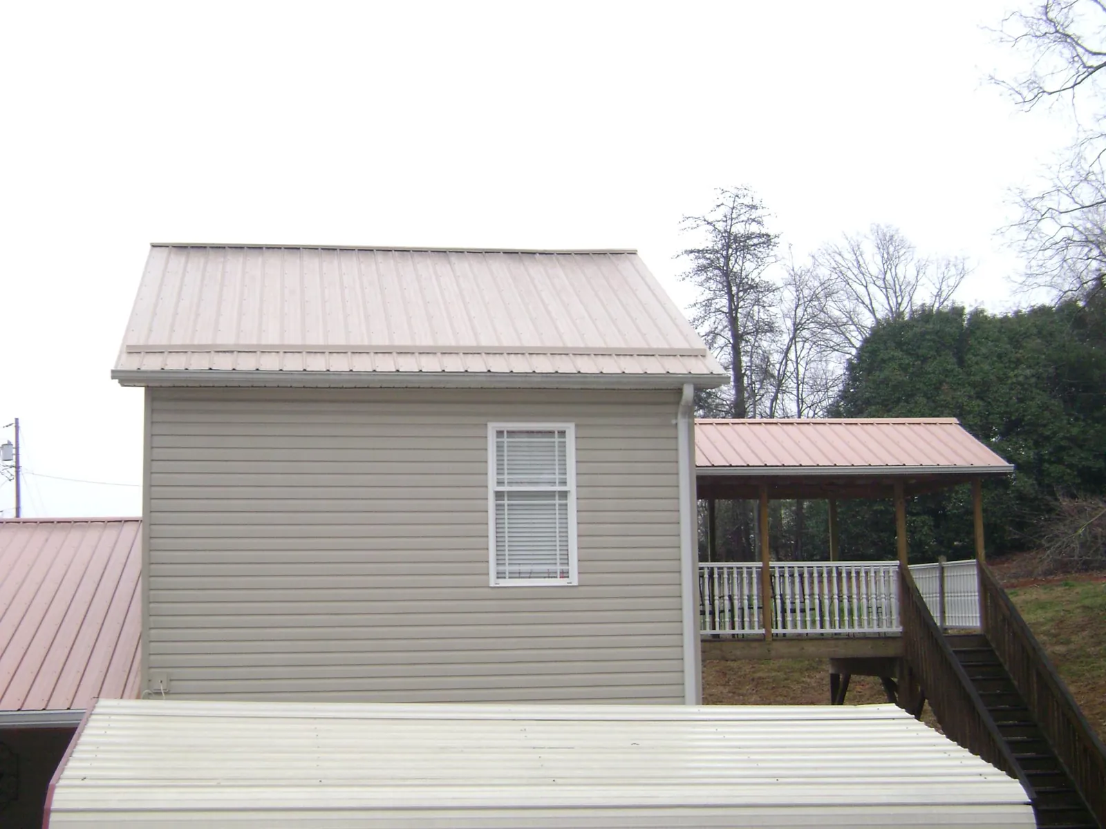 Tan metal roofs on a two story addition and attached porch, from a Roof Replacement job in Mineral Wells